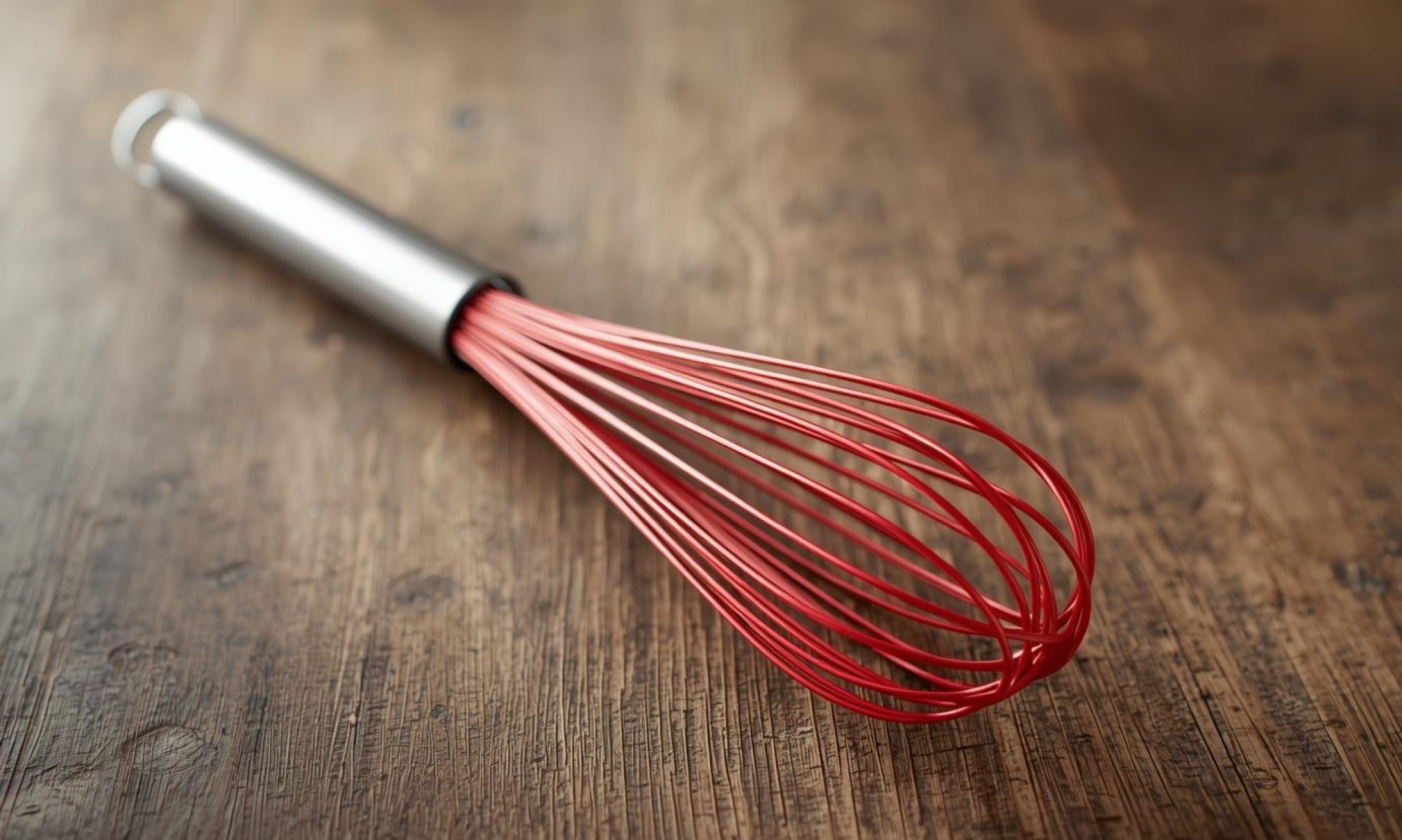 Red whisk on a rustic wood table.